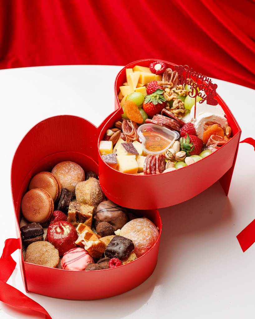 Heart-shaped red gift box filled with assorted confectionery on a white surface with a red background.