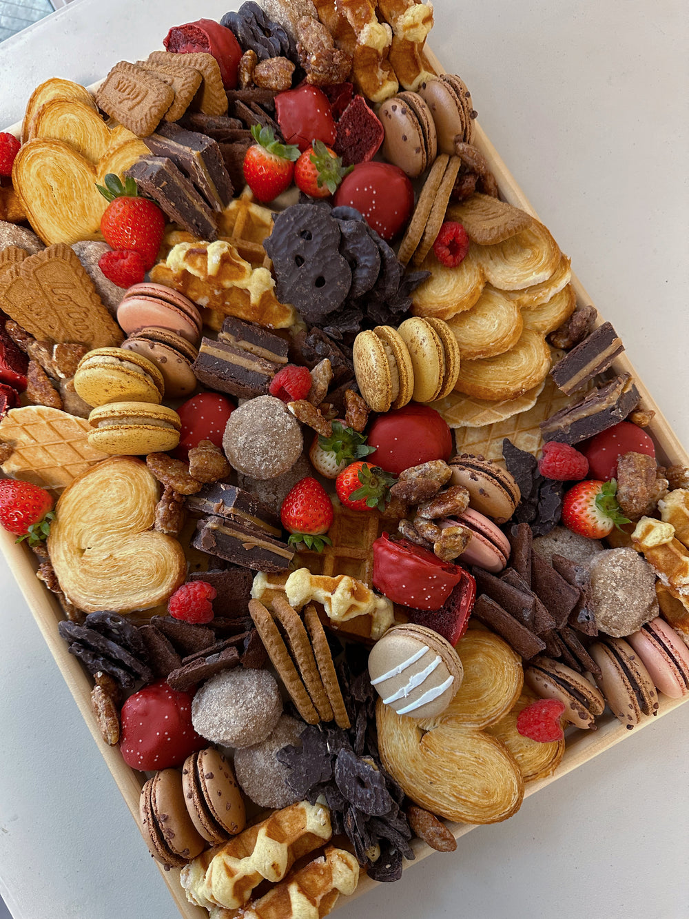 Assorted small snacks including cookies, macarons, and fruits arranged in a heart shape on a white plate.